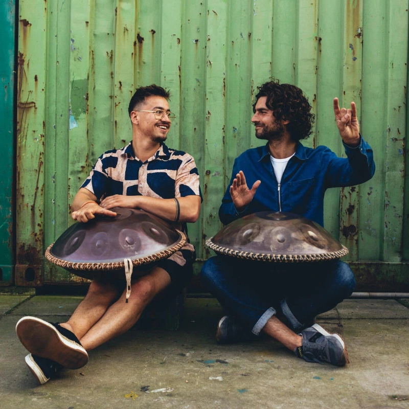 A pair of handpan enthusiasts immersed in music-making in a tranquil open-air location.