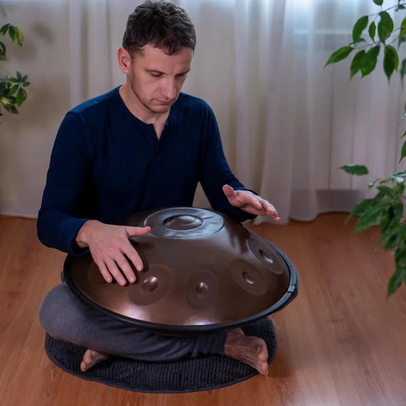 A musician concentrating on playing the handpan drum in a cozy indoor setting.