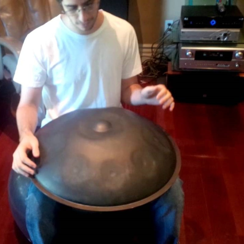 A male musician immersed in the process of recording the resonant tones of a hang instrument in a soundproof home studio.