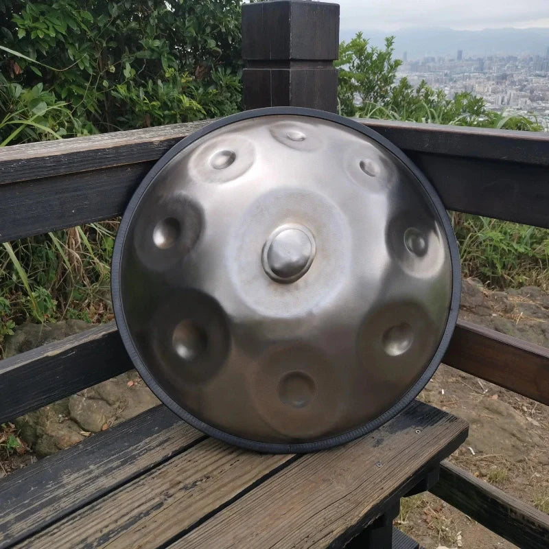 A silver handpan resting on a park bench, surrounded by greenery.