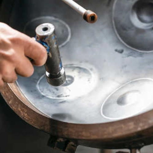 A skilled tuner meticulously shaping a handpan in a workshop filled with tools